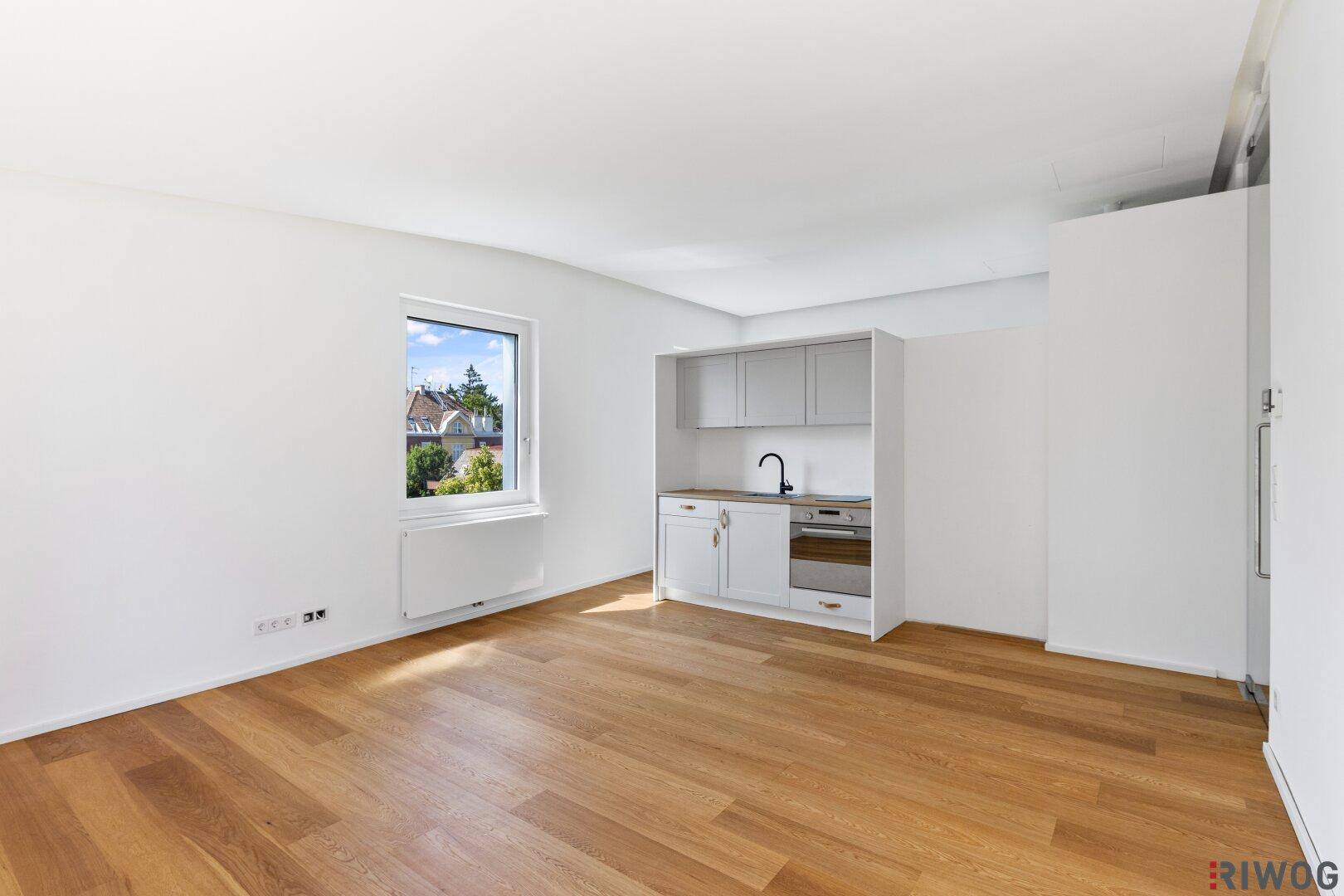 Heller Raum mit Kochnische, Holzboden und Fenster mit Ausblick.