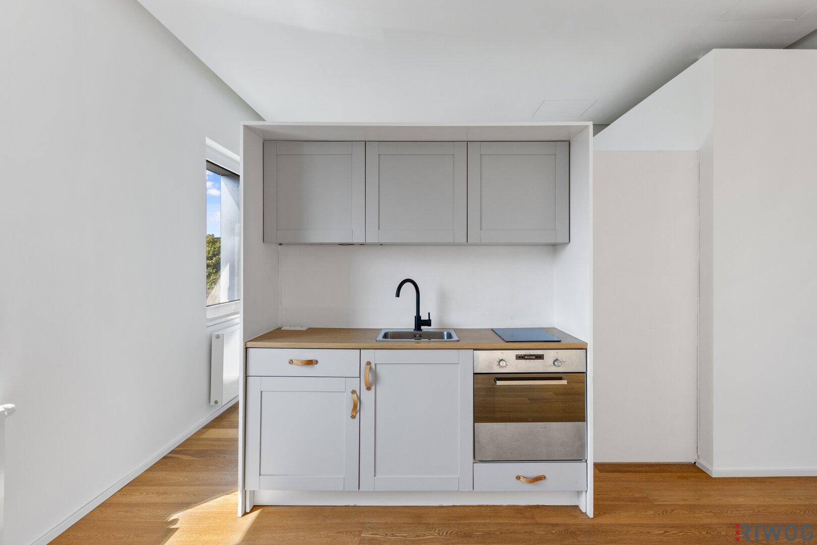 Moderne Kochnische mit grauen Schränken, Holzarbeitsplatte und integriertem Backofen.