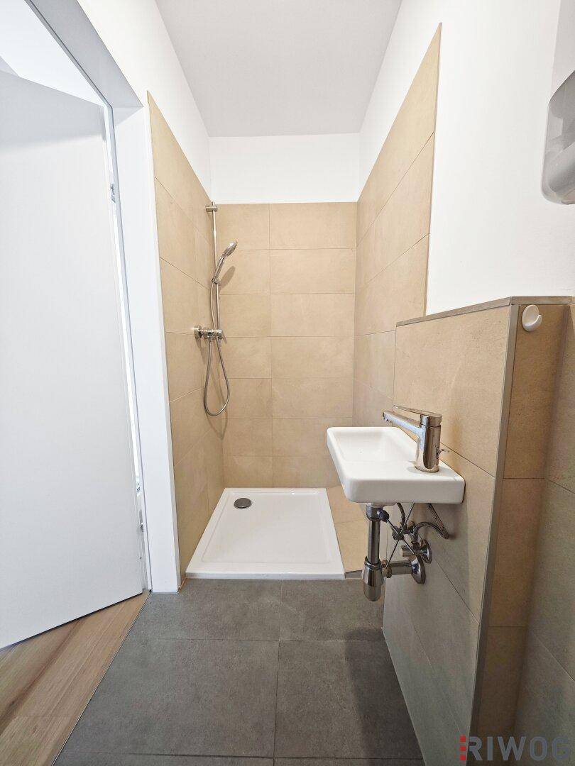 Kleines Badezimmer mit Duschbereich, beigefarbenen Wandfliesen und grauem Boden.