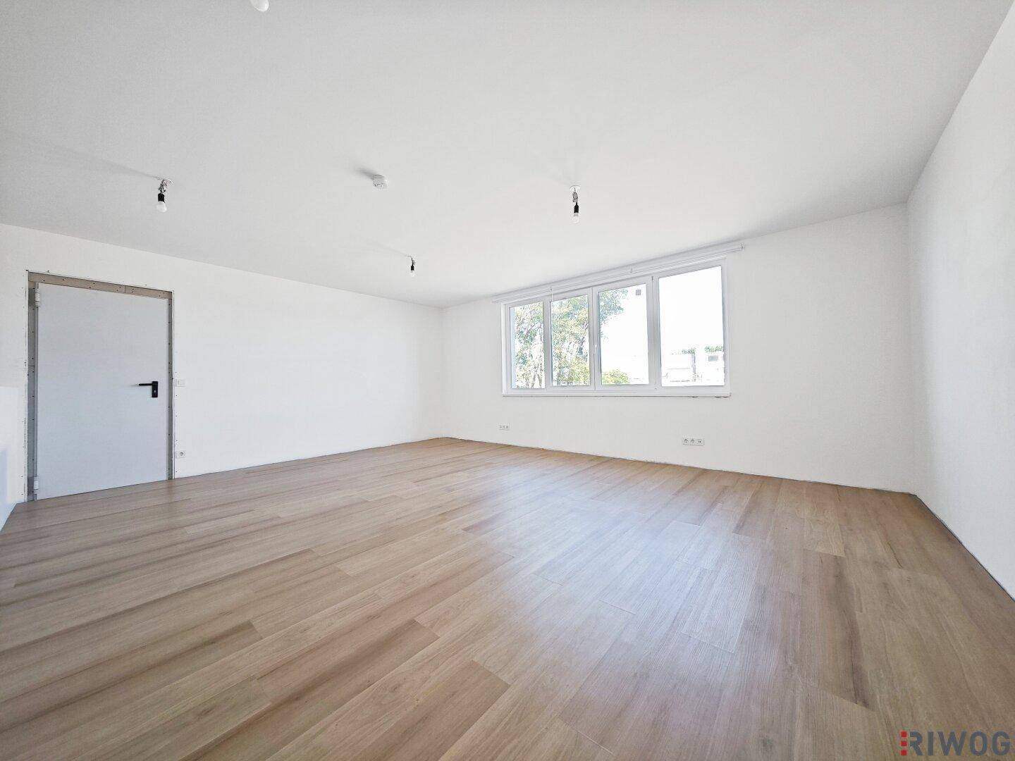 Heller Büroraum mit Holzboden, weißen Wänden und großen Fenstern, die viel Licht hereinlassen.