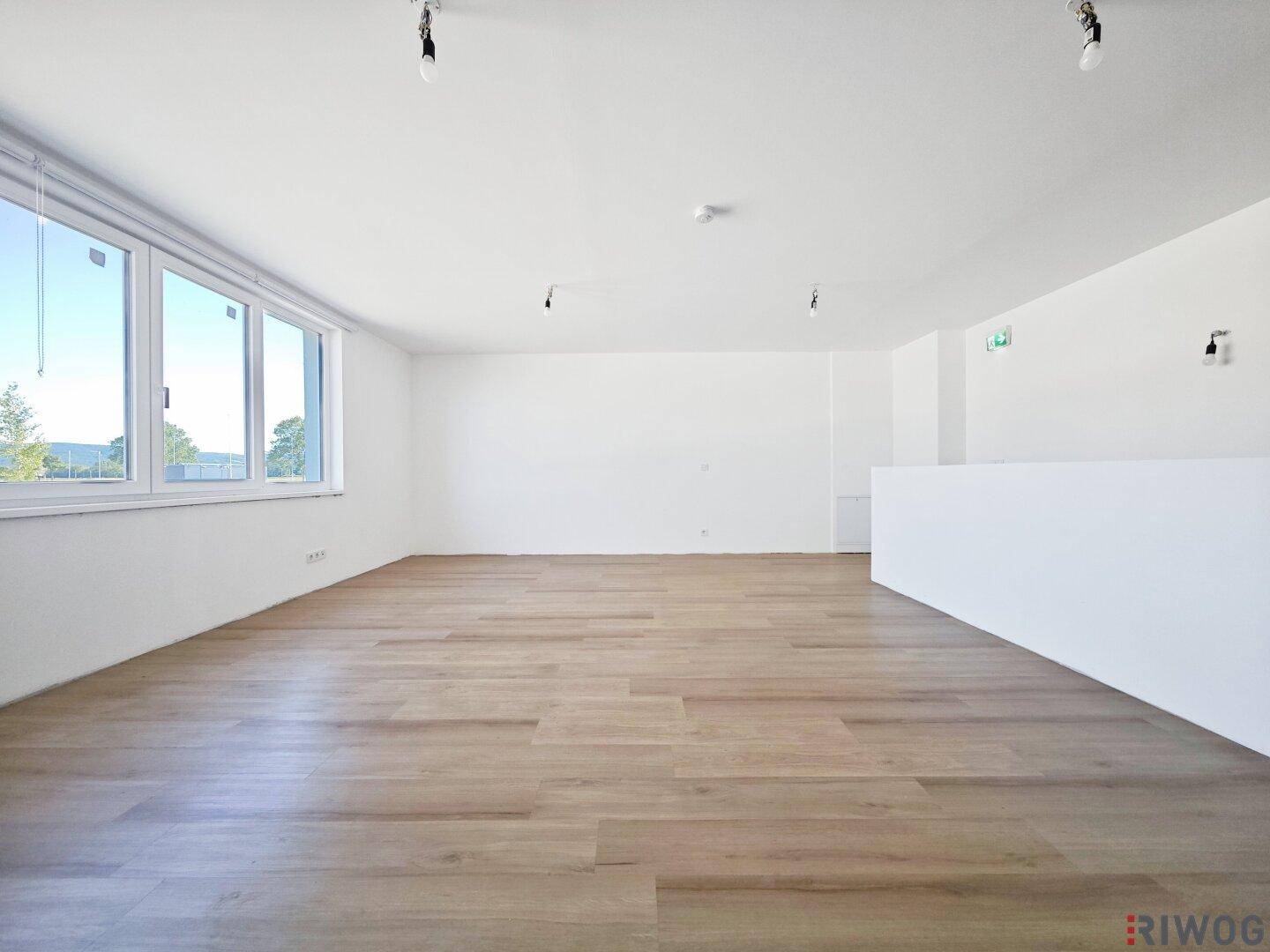 Geräumiger, heller Raum mit Holzboden und großen Fenstern, bietet vielseitige Nutzungsmöglichkeiten.