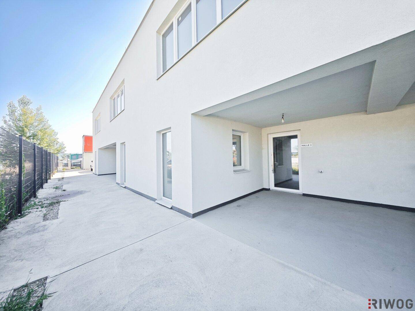 Moderne weiße Gebäudefassade mit großen Fenstern und einem überdachten Eingangsbereich.