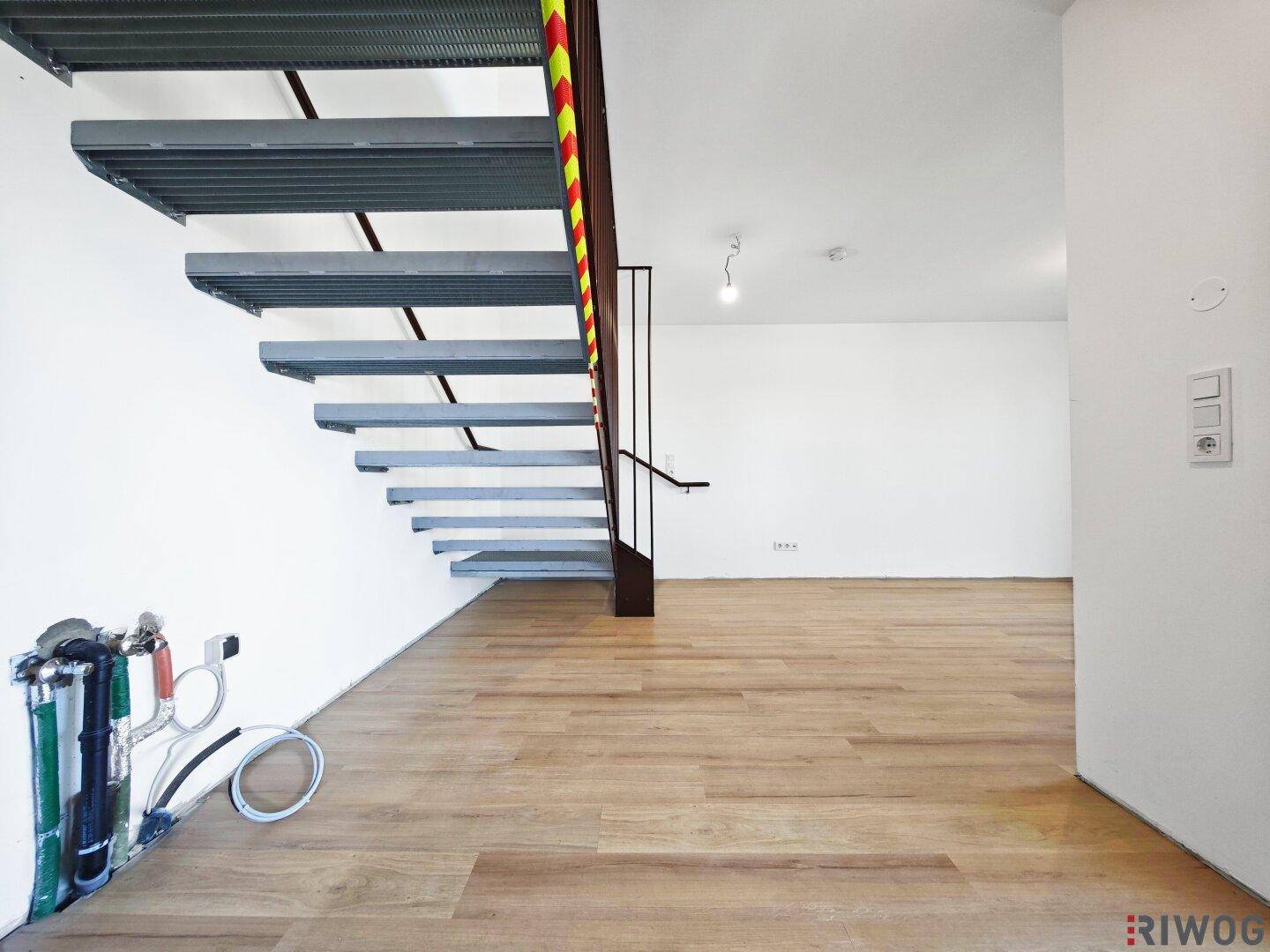Leerer Raum mit Holzboden und einer modernen Metalltreppe, die in die obere Etage führt.