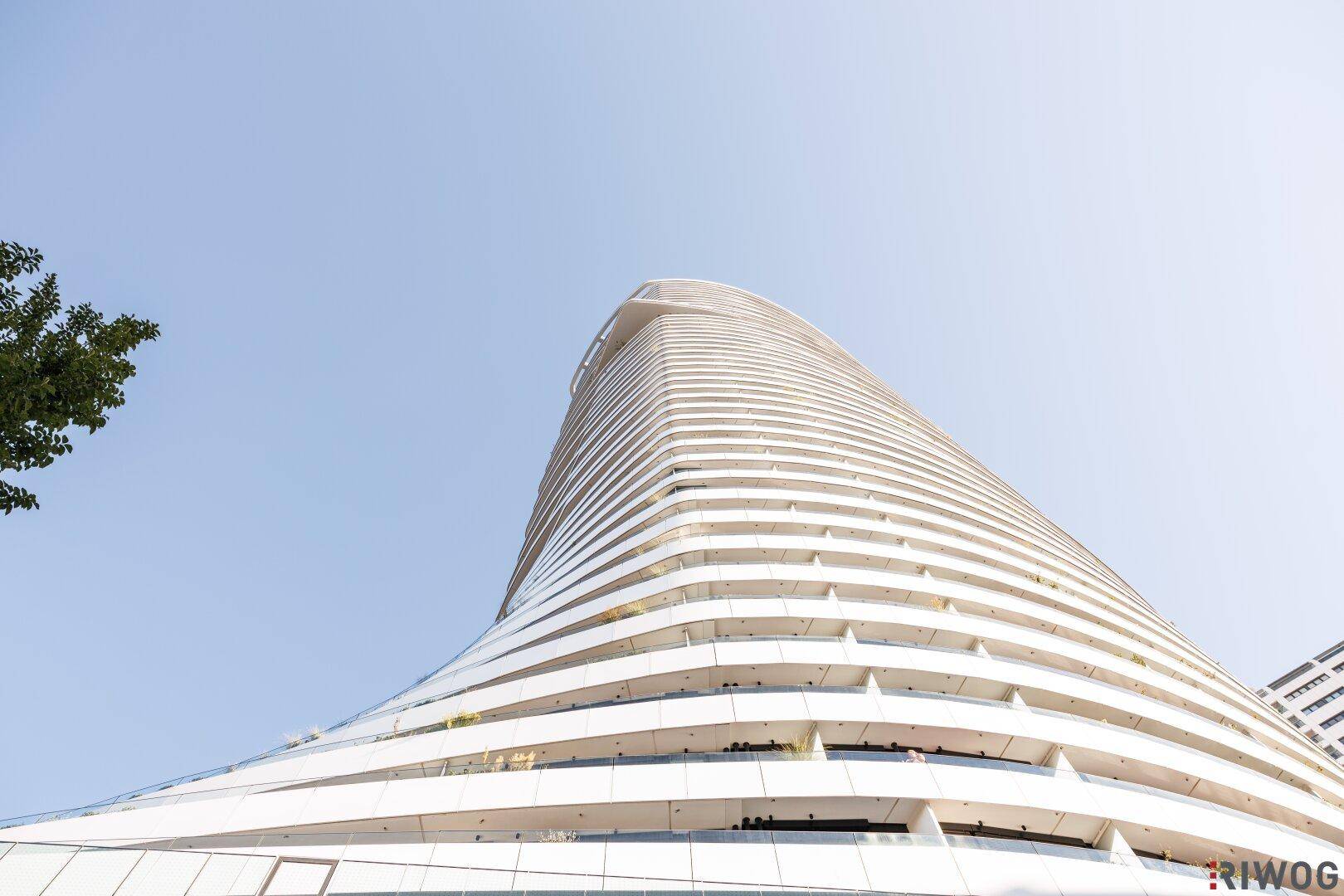 Beeindruckendes, modernes Hochhaus mit geschwungener weißer Fassade unter blauem Himmel.