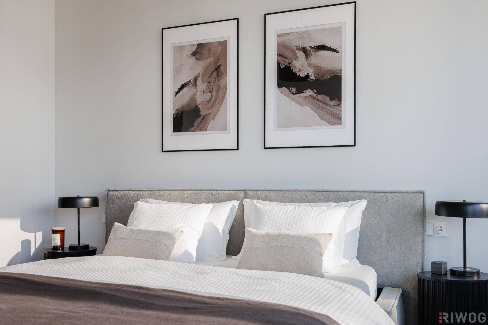 Helles Schlafzimmer mit bequemen Bett, Nachttischen und stilvollen Bildern über dem Kopfteil.