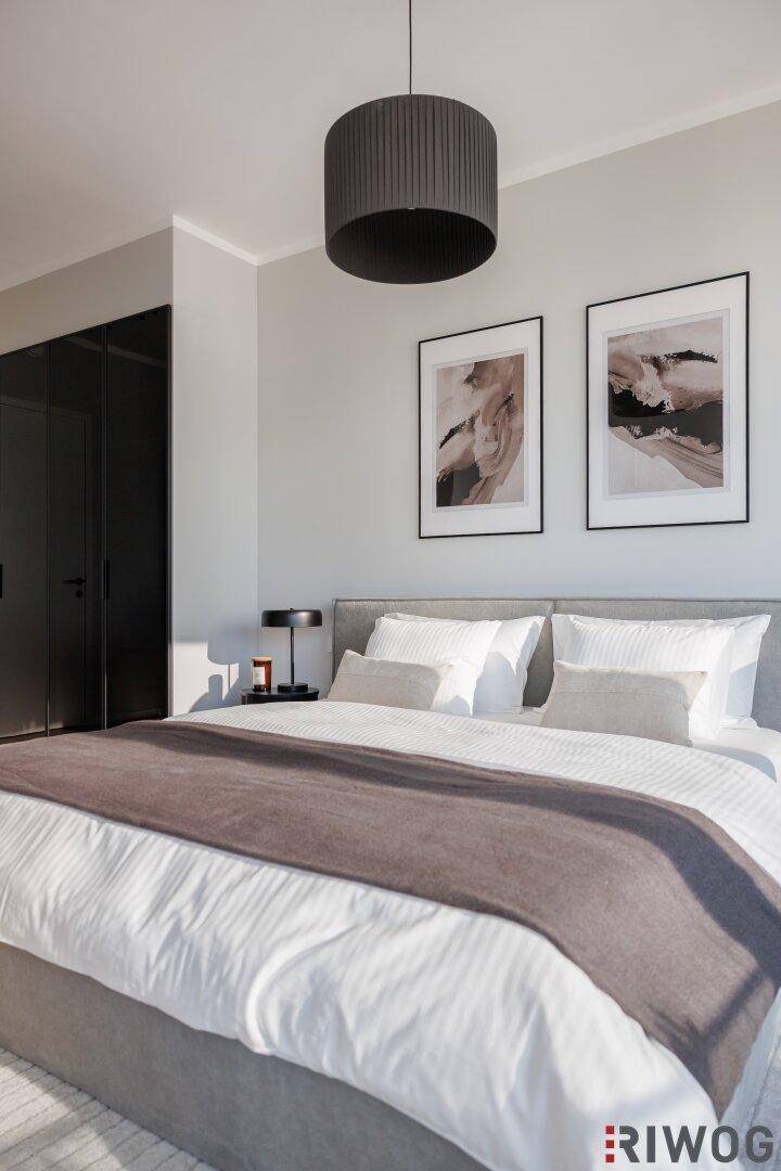 Elegantes Schlafzimmer mit großem Bett, moderner Deckenleuchte und dunklen Einbauschränken.
