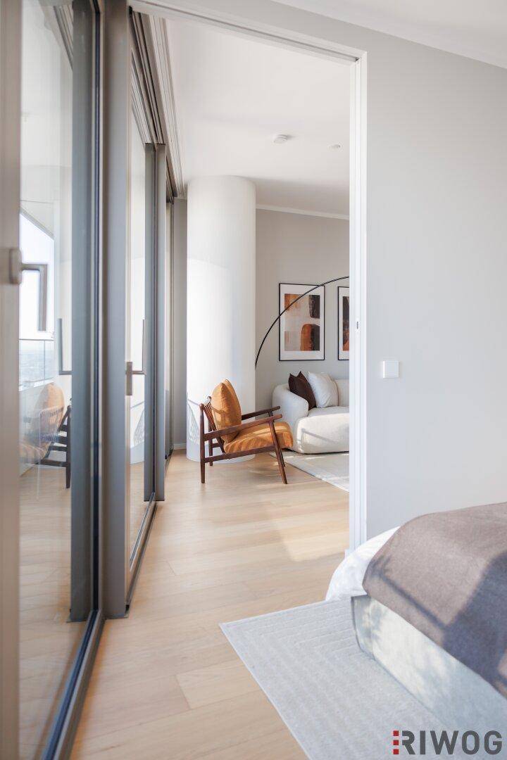Blick vom Schlafzimmer in den hellen Wohnbereich mit Holzboden und großen Fenstern.