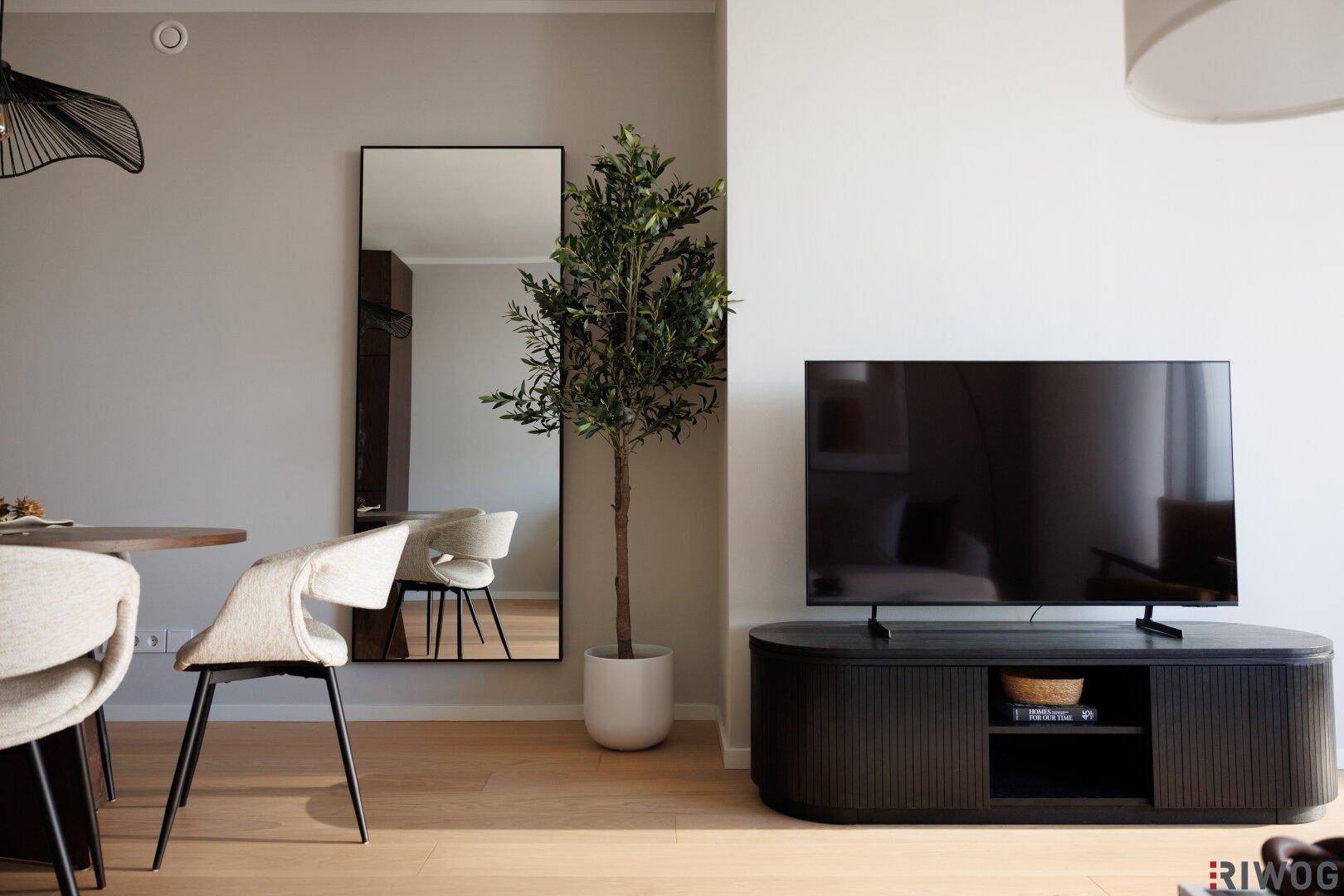 Wohnbereich mit großem Fernseher, stilvollem Sideboard und einer hohen Pflanze.