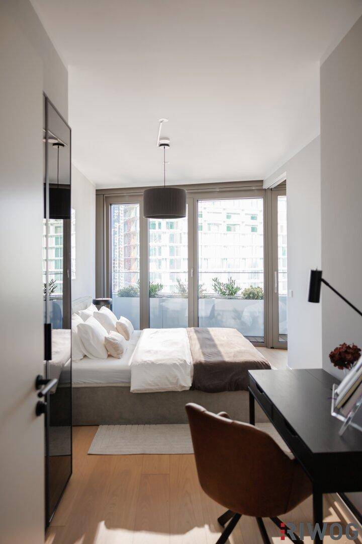 Helles Schlafzimmer mit großem Fenster, Schreibtisch und Zugang zu einem Außenbereich.