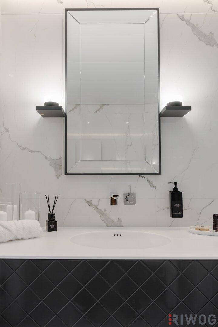 Elegantes Badezimmer mit Marmorwänden, modernem Waschtisch und beleuchtetem Spiegel.