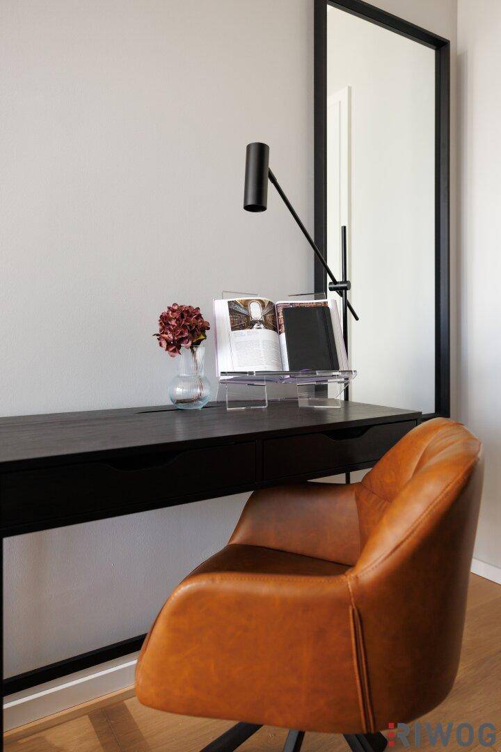 Detailaufnahme des Schreibtisches mit Lampe, Buchständer und bequemem Ledersessel.