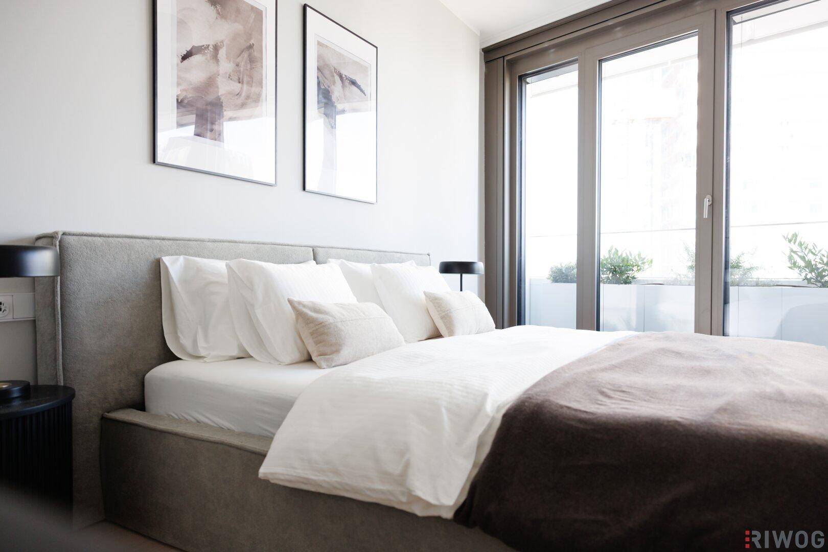 Modernes Schlafzimmer mit großem Bett, Kunstwerken und bodentiefen Fenstern für viel Licht.