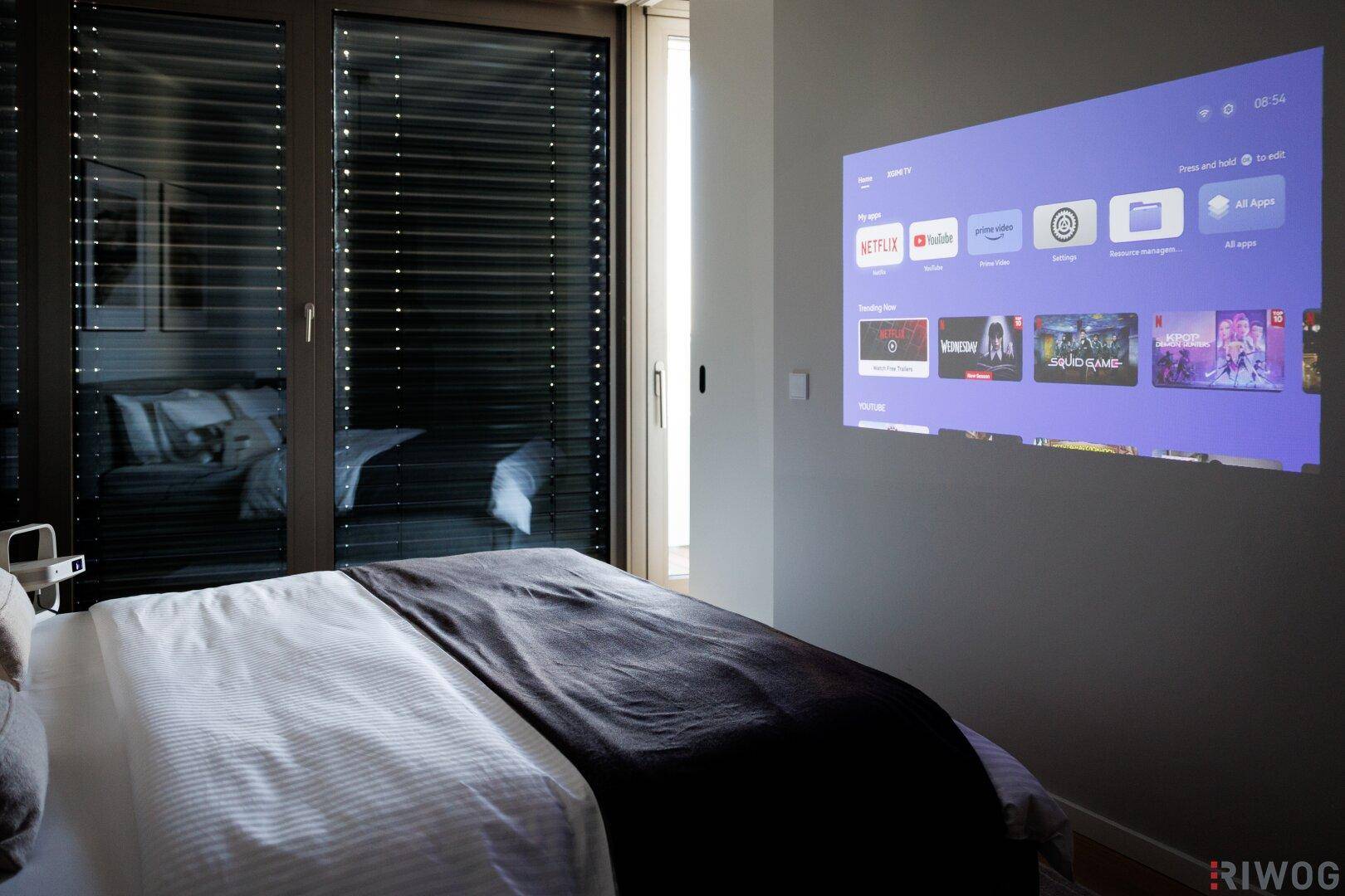 Gemütliches Schlafzimmer mit Projektor an der Wand und großem Bett, ideal für Filmabende.