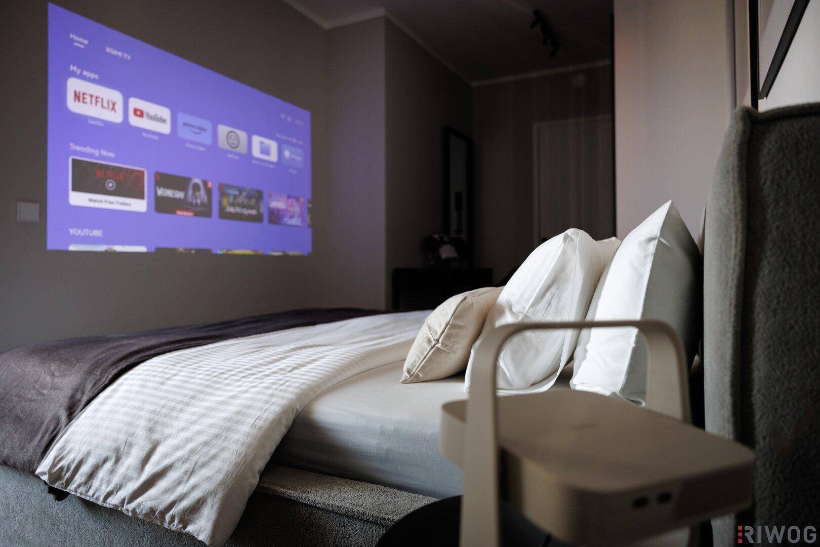 Schlafzimmer mit Projektor, bequemen Bett und moderner Einrichtung für entspannte Stunden.