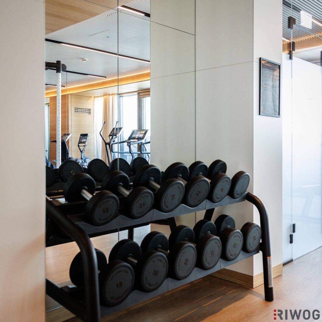 Hantelablage in einem gut ausgestatteten Fitnessraum mit Spiegeln, die weitere Trainingsgeräte reflektieren.