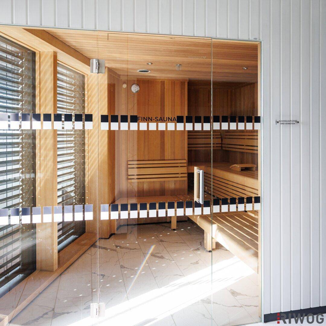 Moderne Finn-Sauna mit Holzverkleidung und Bänken, zugänglich durch eine Glastür im Wellnessbereich.
