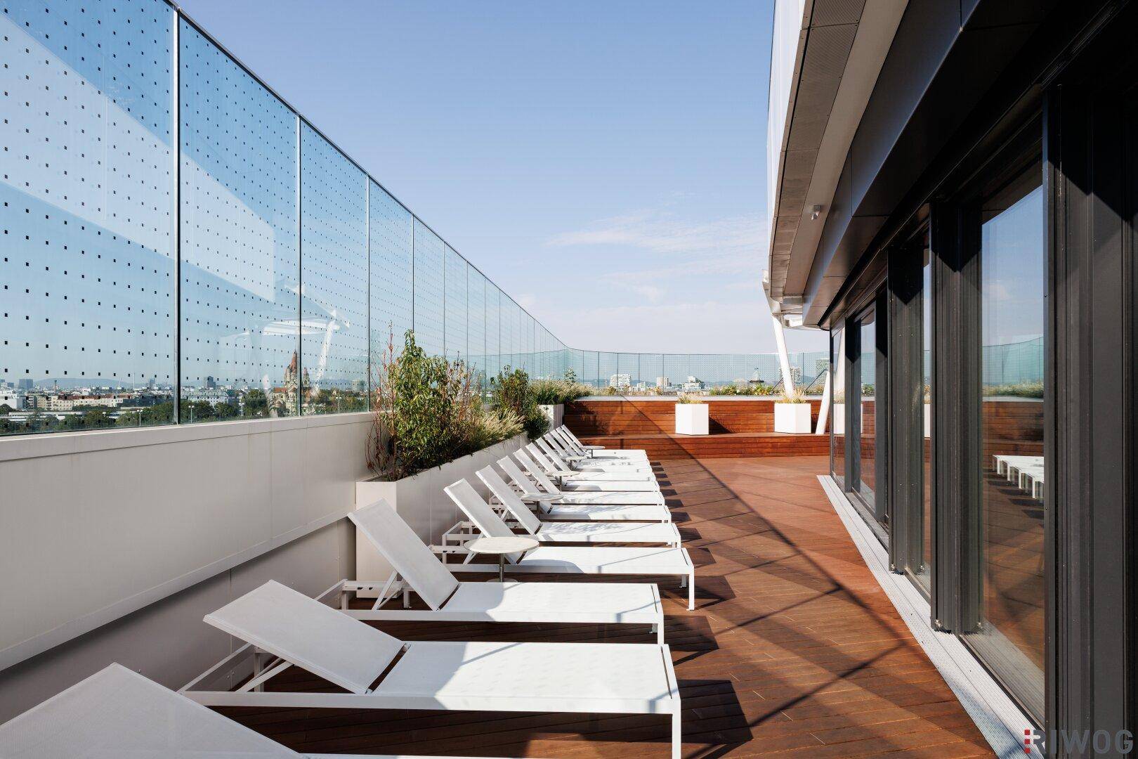 Großzügige Dachterrasse mit zahlreichen Liegestühlen, Holzdeck und Glasgeländer für Entspannung.