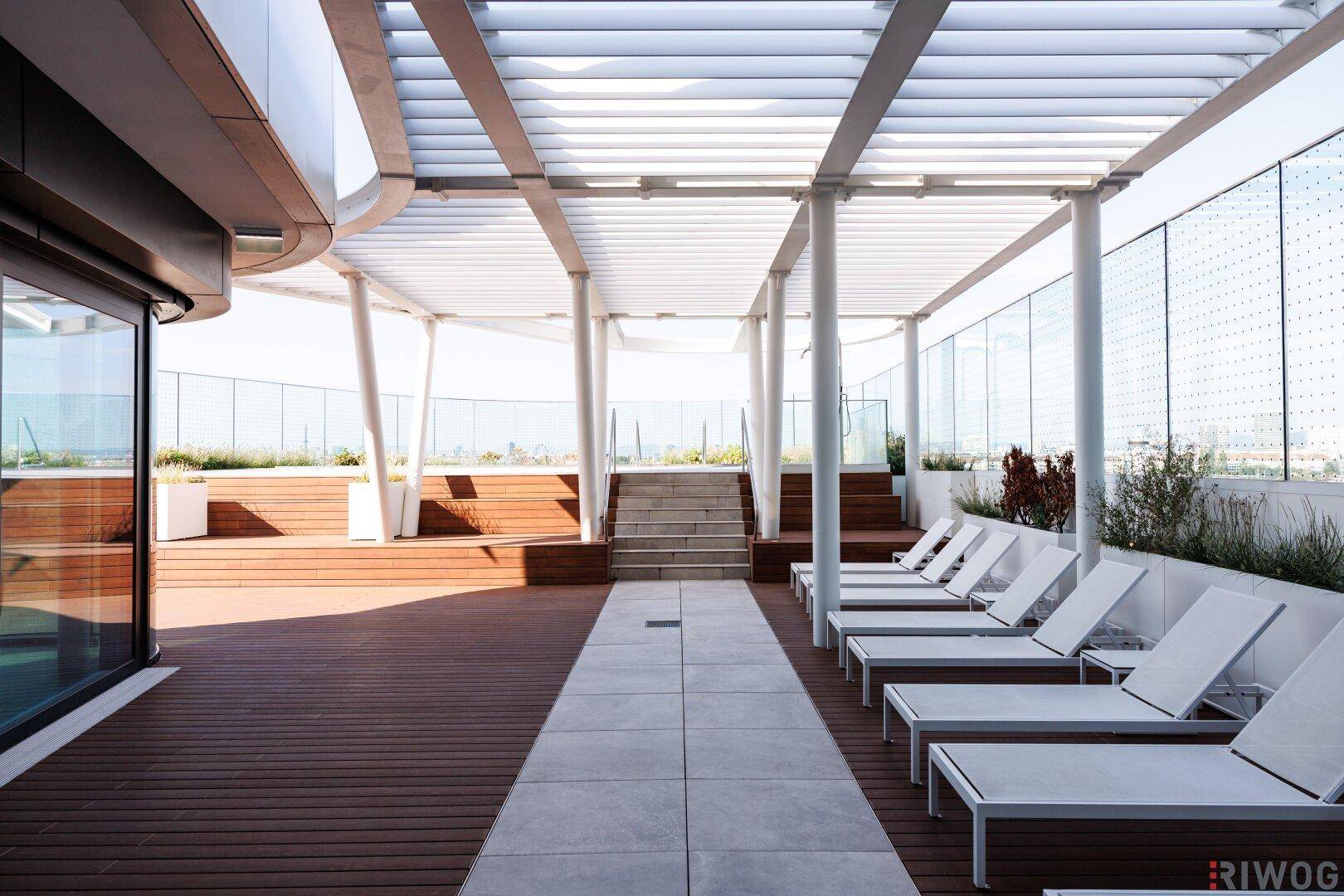 Weitläufige Dachterrasse mit Pergola, Liegestühlen und Holzdeck, ideal zum Entspannen im Freien.