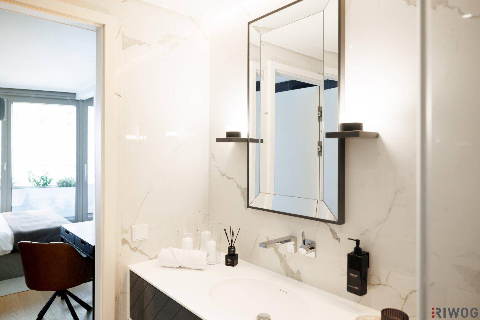 Modernes Badezimmer mit Marmorfliesen, elegantem Waschtisch und großem Spiegel.