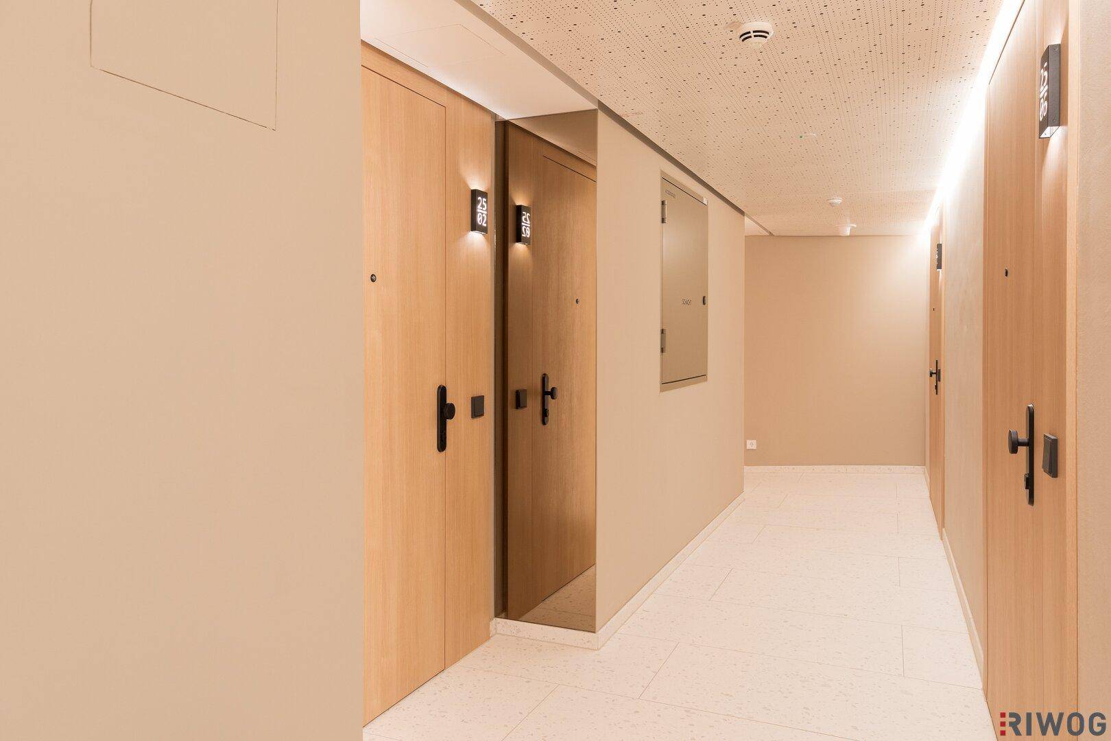 Langer Flur mit Holztüren und moderner Beleuchtung, die den Weg zu den Zimmern erhellt.