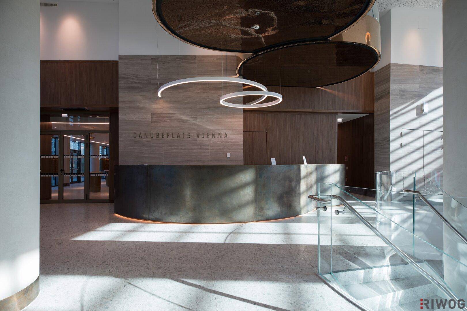 Eindrucksvolle Lobby mit Rezeption, moderner Beleuchtung und einer eleganten Treppe mit Glasgeländer.