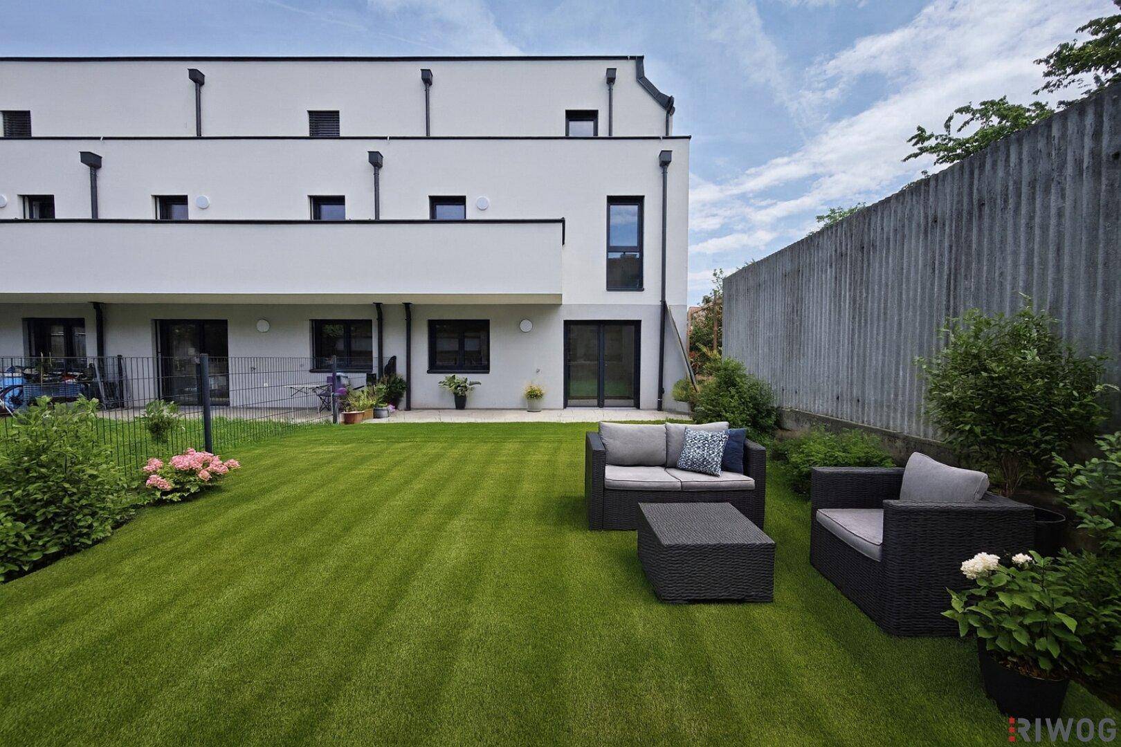 Gepflegter Gartenbereich mit Rasenfläche und moderner Sitzgruppe hinter dem Gebäude.