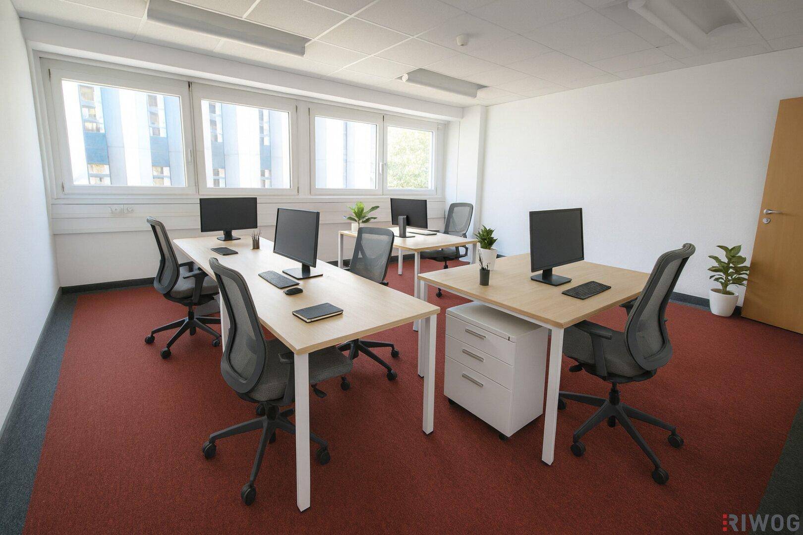 Modernes Büro mit mehreren Arbeitsplätzen, roten Teppichfliesen und Blick auf andere Gebäude.