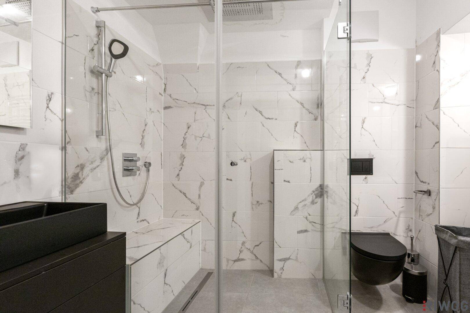 Modernes Badezimmer mit großer begehbarer Dusche, schwarzen Armaturen und Marmorfliesen.