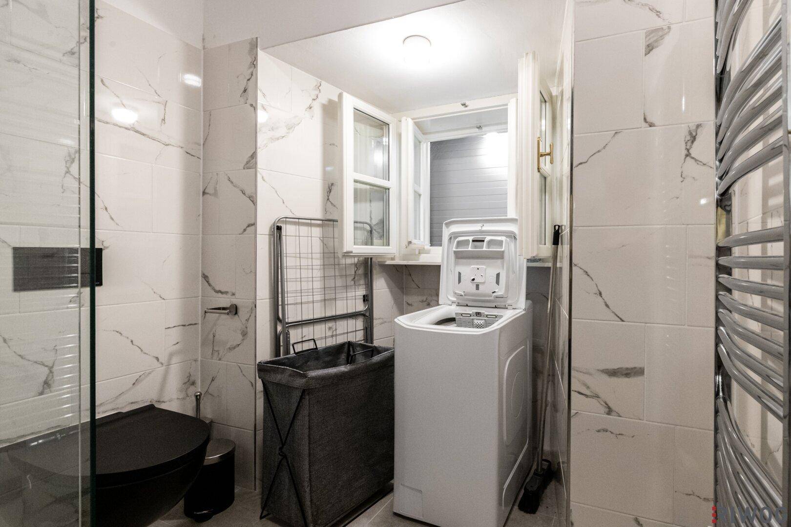 Helles Badezimmer mit Waschmaschine, Fenster, beheiztem Handtuchhalter und modernen Marmorfliesen.