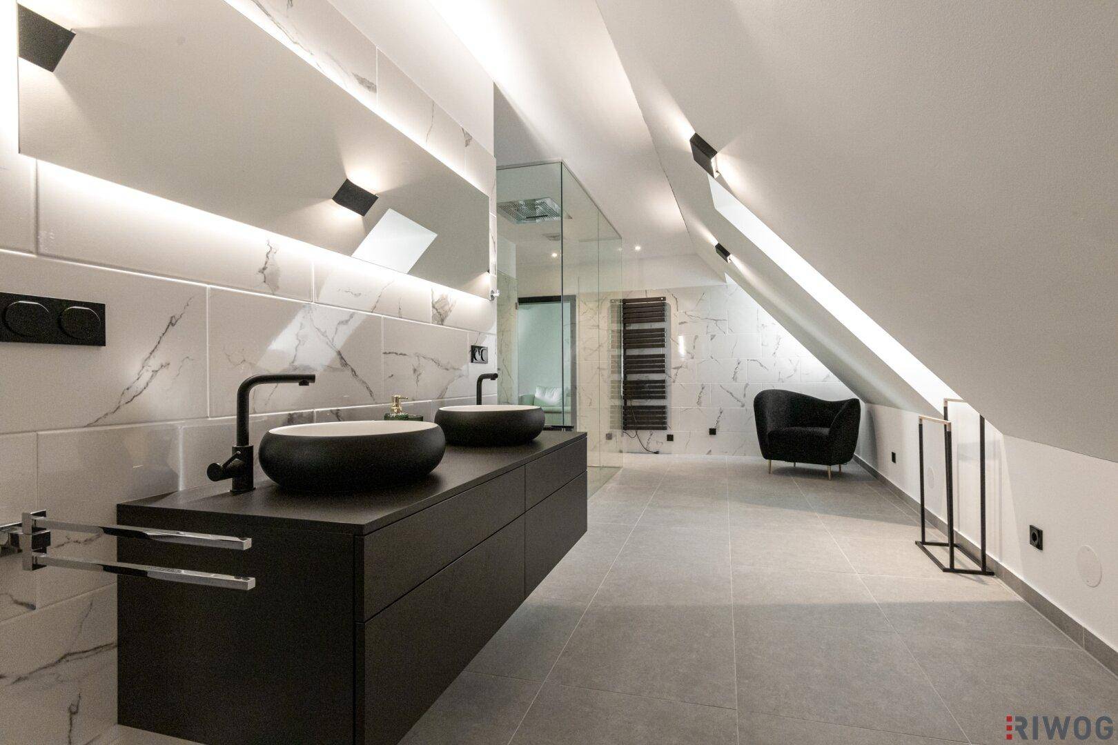 Elegantes Badezimmer mit Doppelwaschbecken, Marmorfliesen und moderner Beleuchtung unter Dachschrägen.