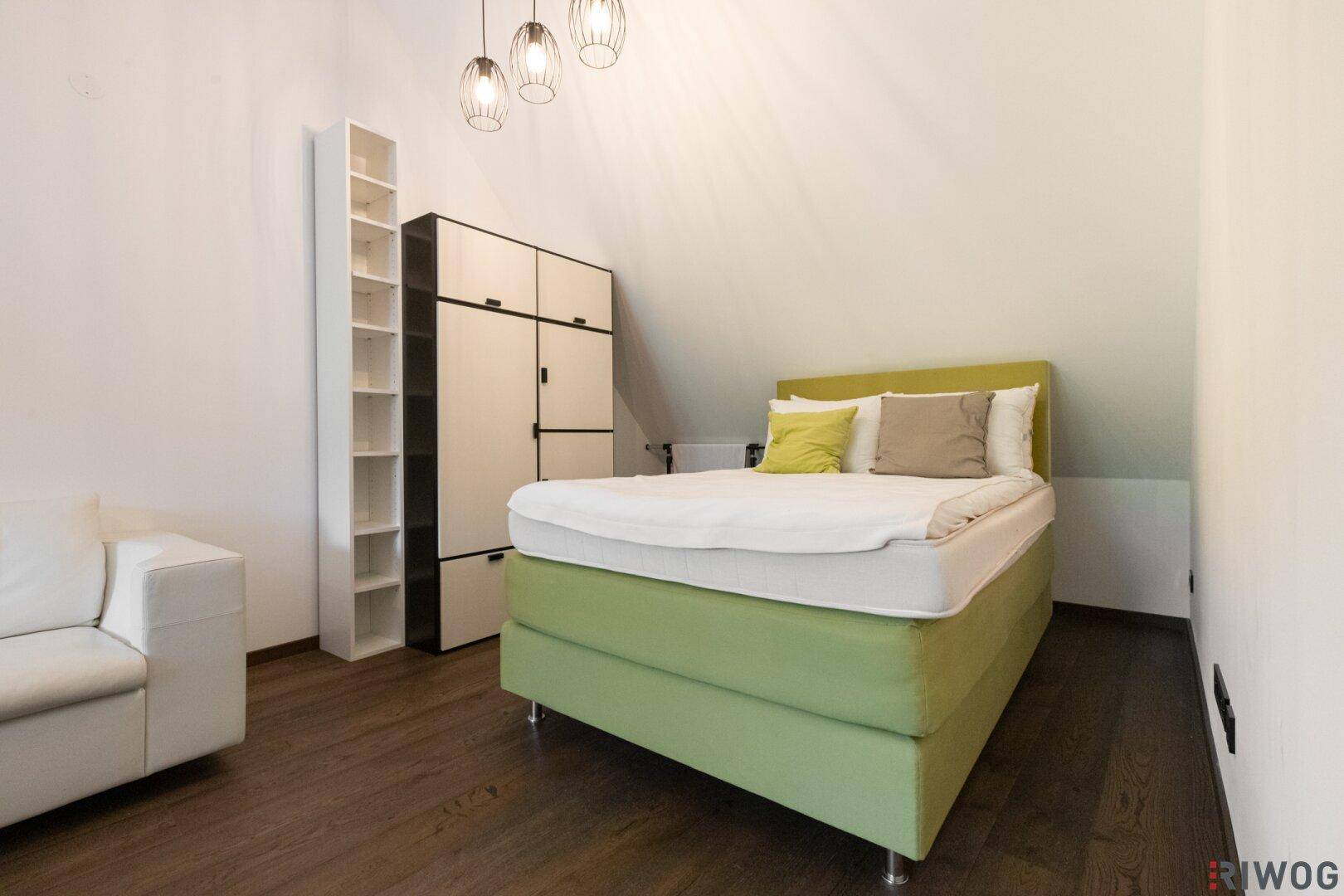 Helles Schlafzimmer mit grünem Bett, Holzboden und praktischen Regalen unter Dachschrägen.