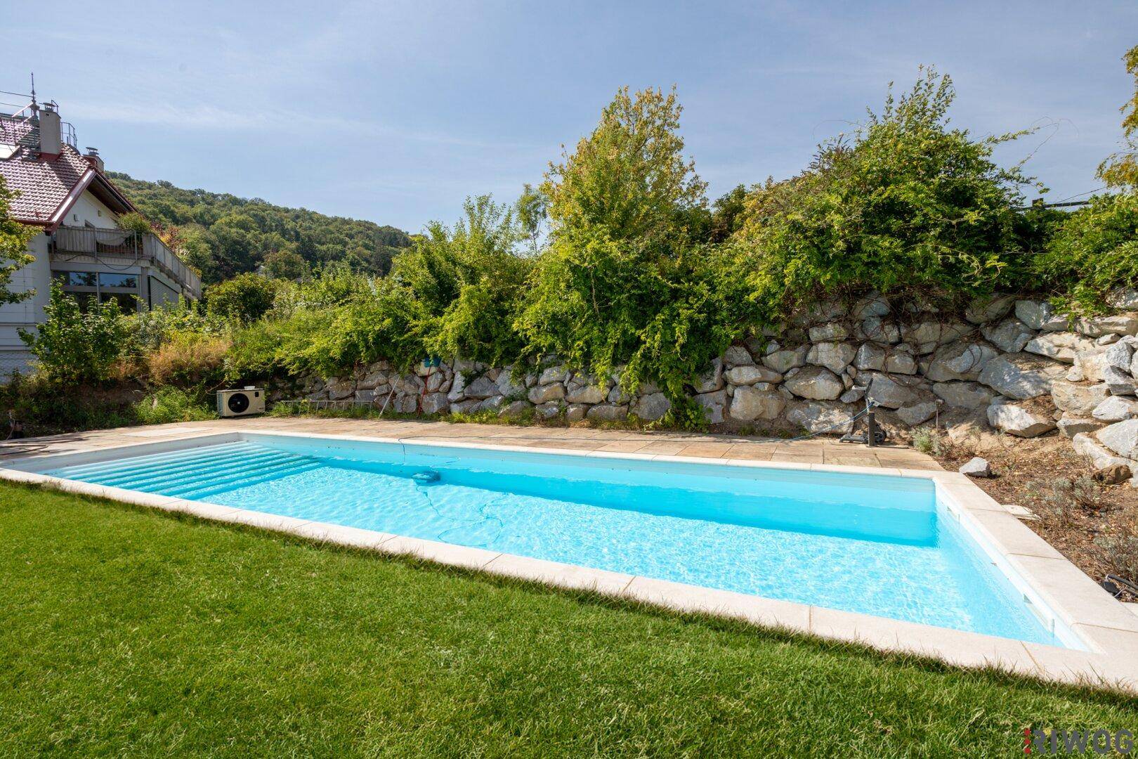 Gepflegter Garten mit großem Swimmingpool, Rasenfläche und einer Natursteinmauer.