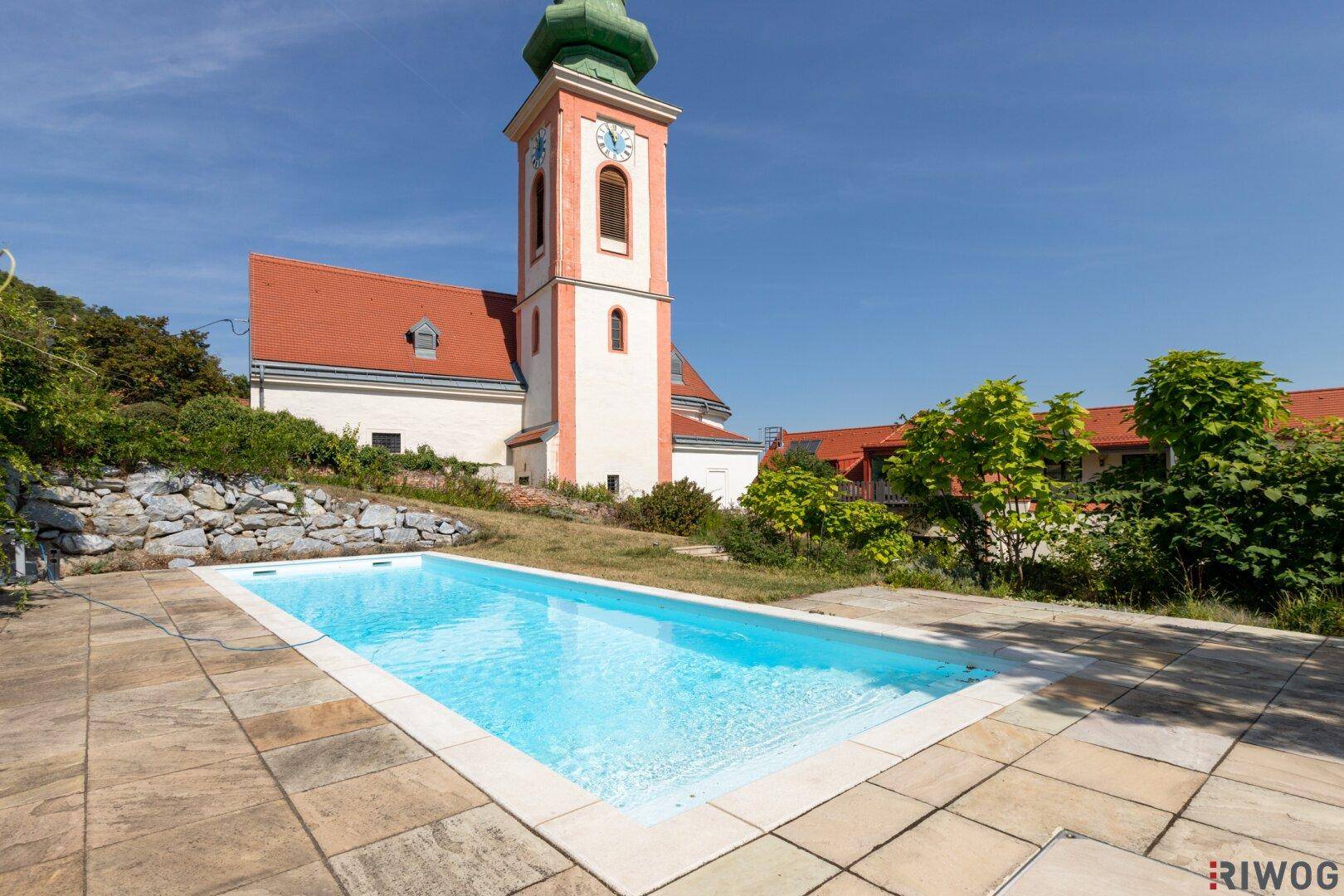 Außenpool mit gepflasterter Terrasse und malerischem Blick auf eine historische Kirche.