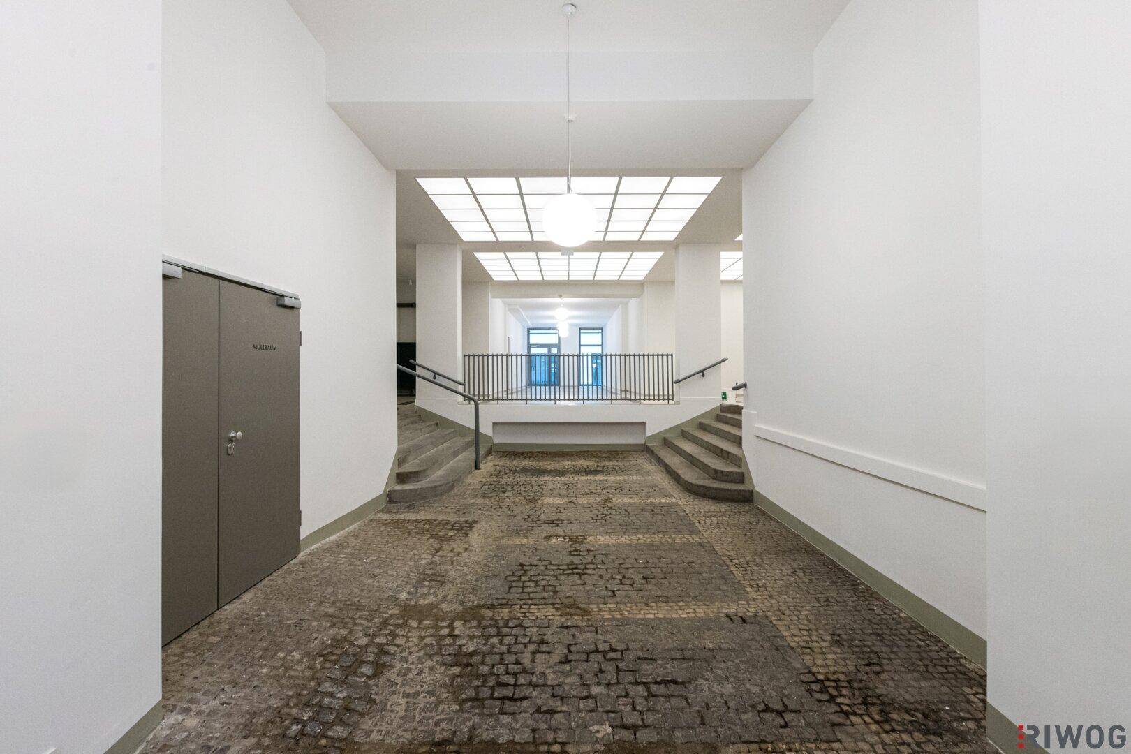 Geräumiger Eingangsbereich mit hohen Decken, Steinboden und Treppen zu verschiedenen Ebenen.