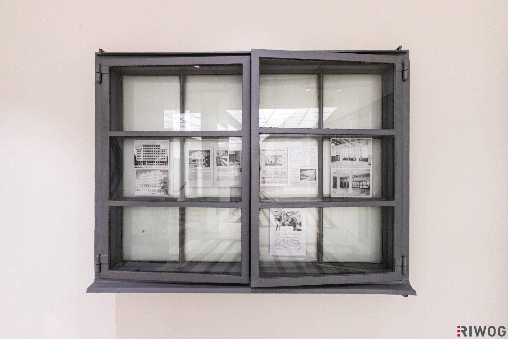 Detailansicht eines Fensters mit historischen Fotos und Dokumenten, eingebettet in die Wand.