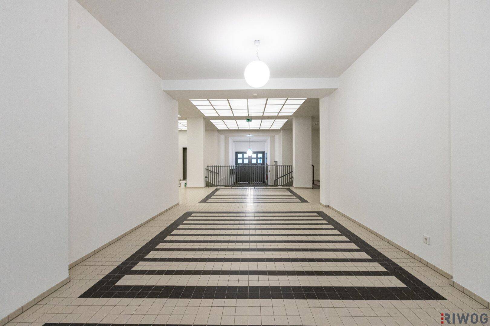 Langer, heller Flur mit markantem Schwarz-Weiß-Fliesenmuster und moderner Deckenbeleuchtung.