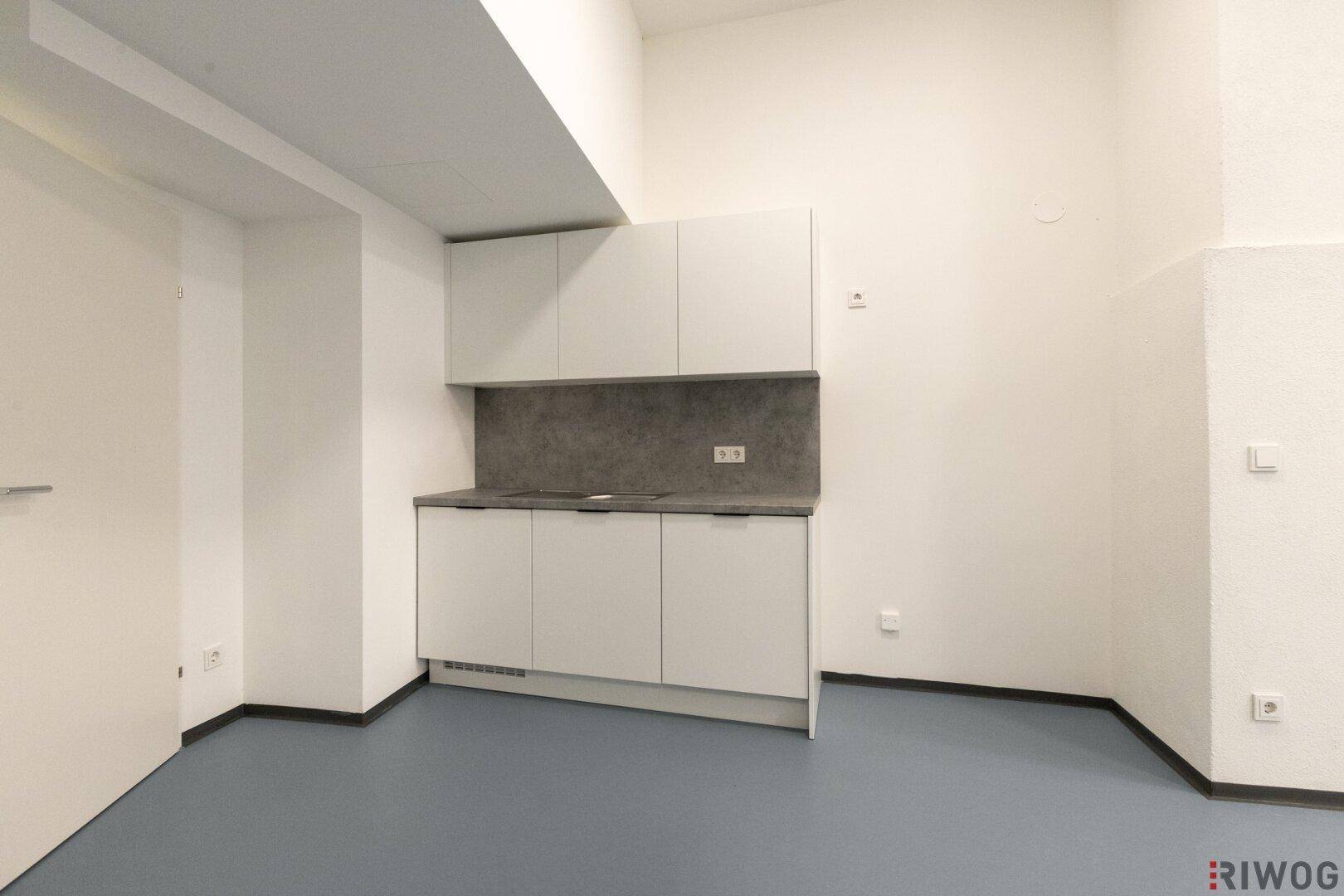 Kompakte Küchenzeile mit weißen Schränken und grauer Arbeitsplatte in einem hellen Raum.