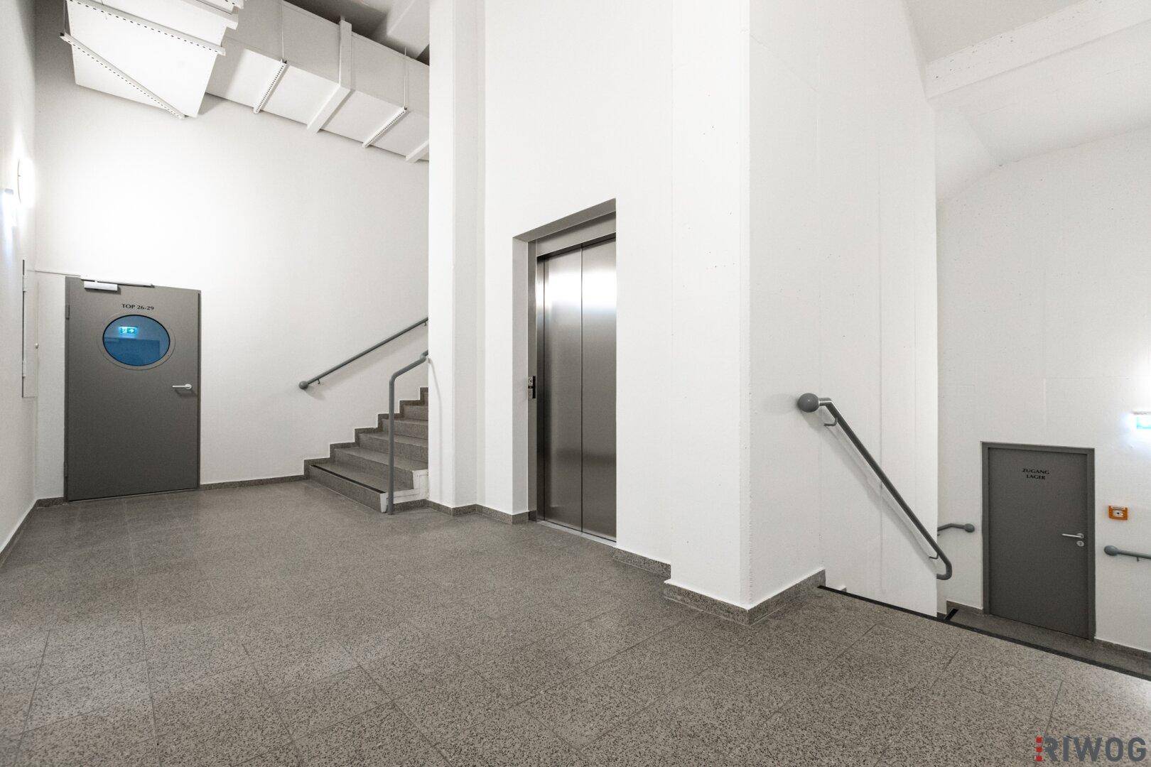 Moderner Aufzug und Treppenhaus in einem hellen Gemeinschaftsbereich mit Fliesenboden.