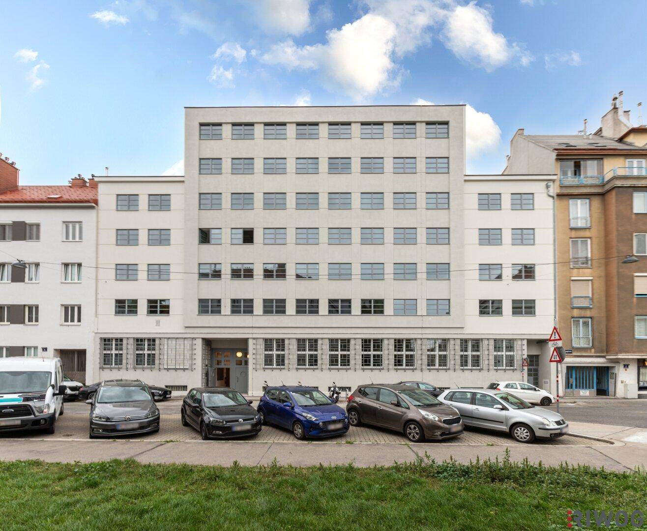 Moderne Gebäudefassade mit vielen Fenstern und Parkplätzen davor.