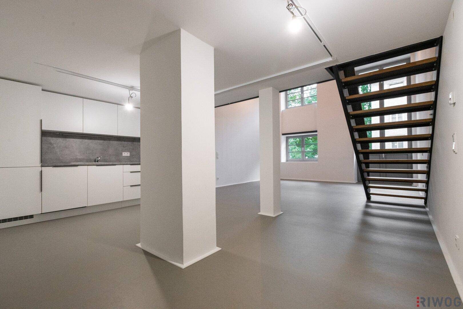 Offener Wohnbereich mit integrierter Küchenzeile, Säulen und Blick nach draußen.