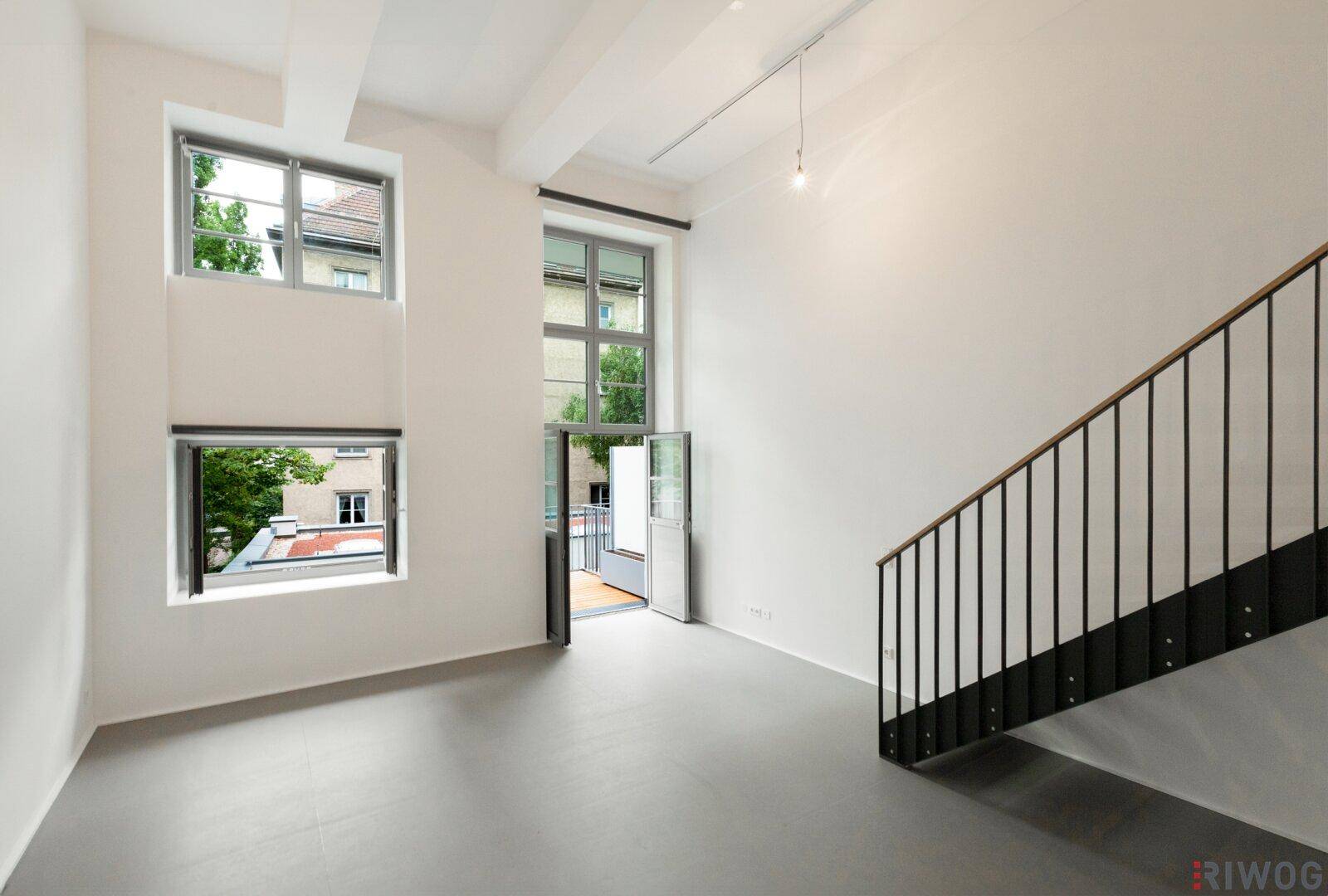 Geräumiger Wohnbereich mit hohen Decken, großen Fenstern und einer modernen Treppe.