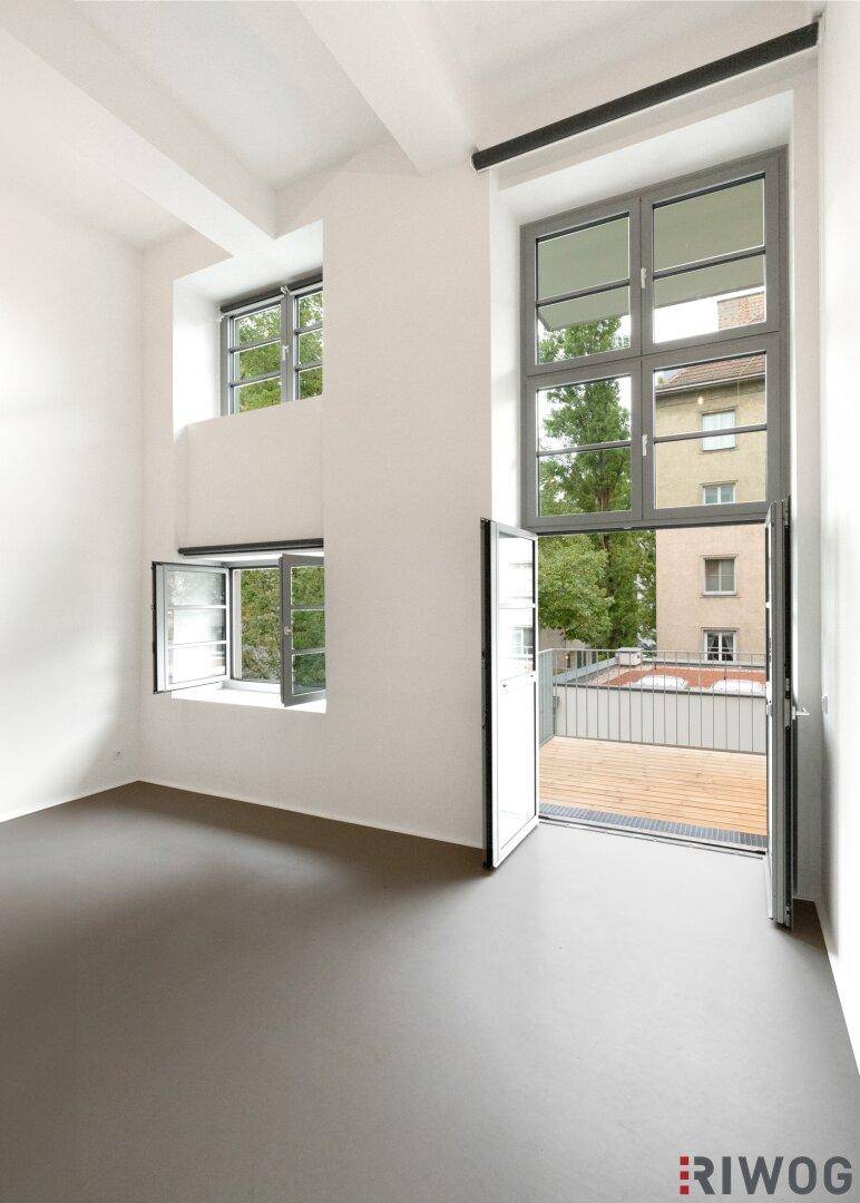 Heller Wohnraum mit hohen Decken, großen Fenstern und direktem Zugang zum Balkon.