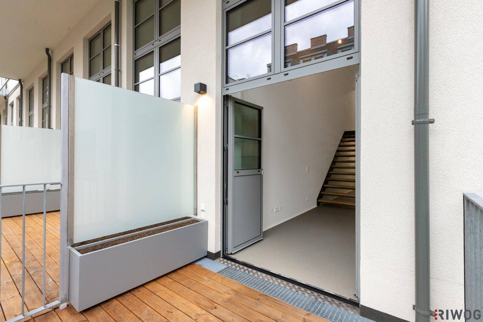 Balkon mit Holzboden und Zugang zum Innenbereich, abgetrennt durch eine Milchglaswand.