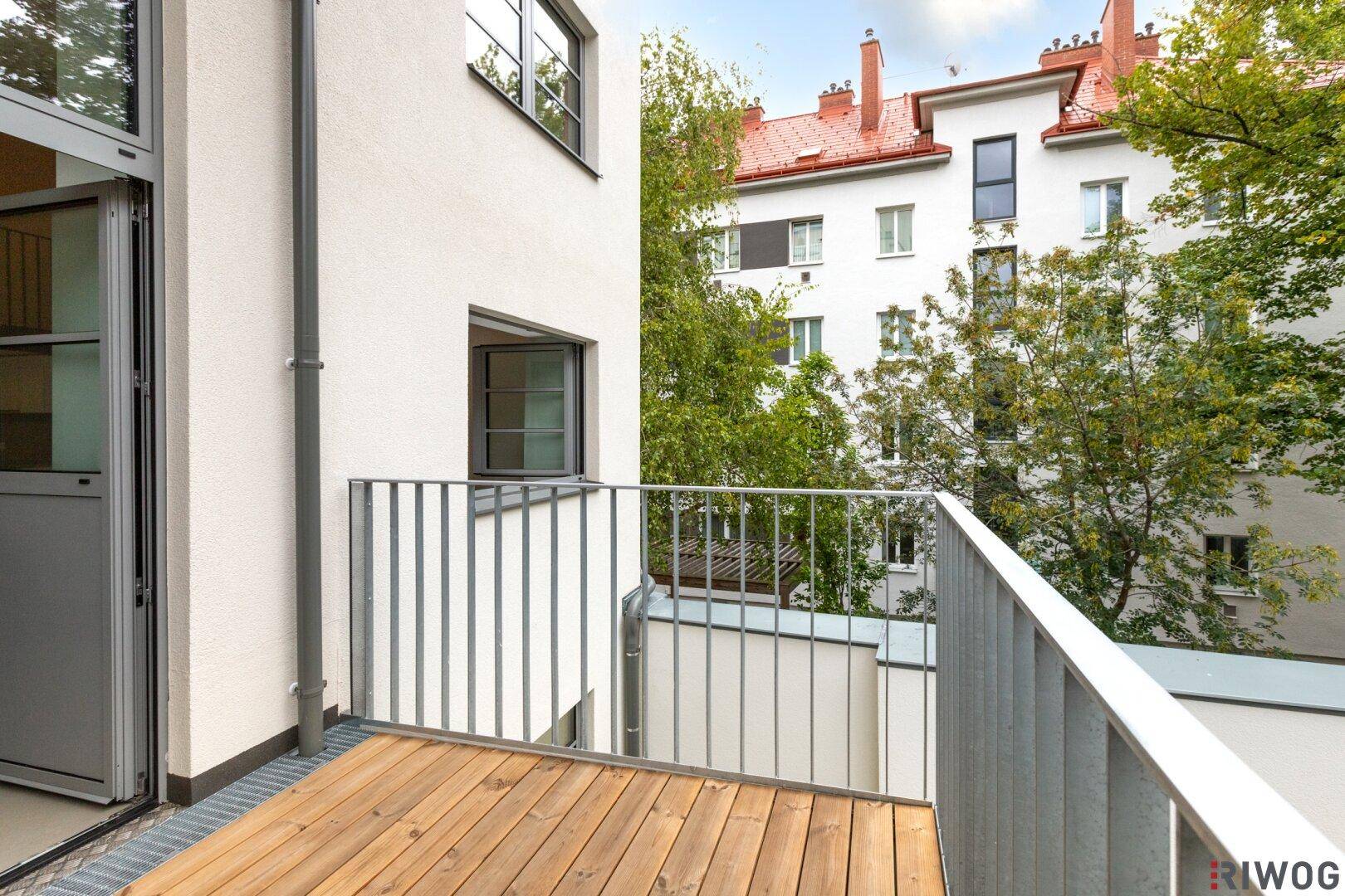 Balkon mit Holzboden und Blick auf die umliegenden Gebäude und Bäume.