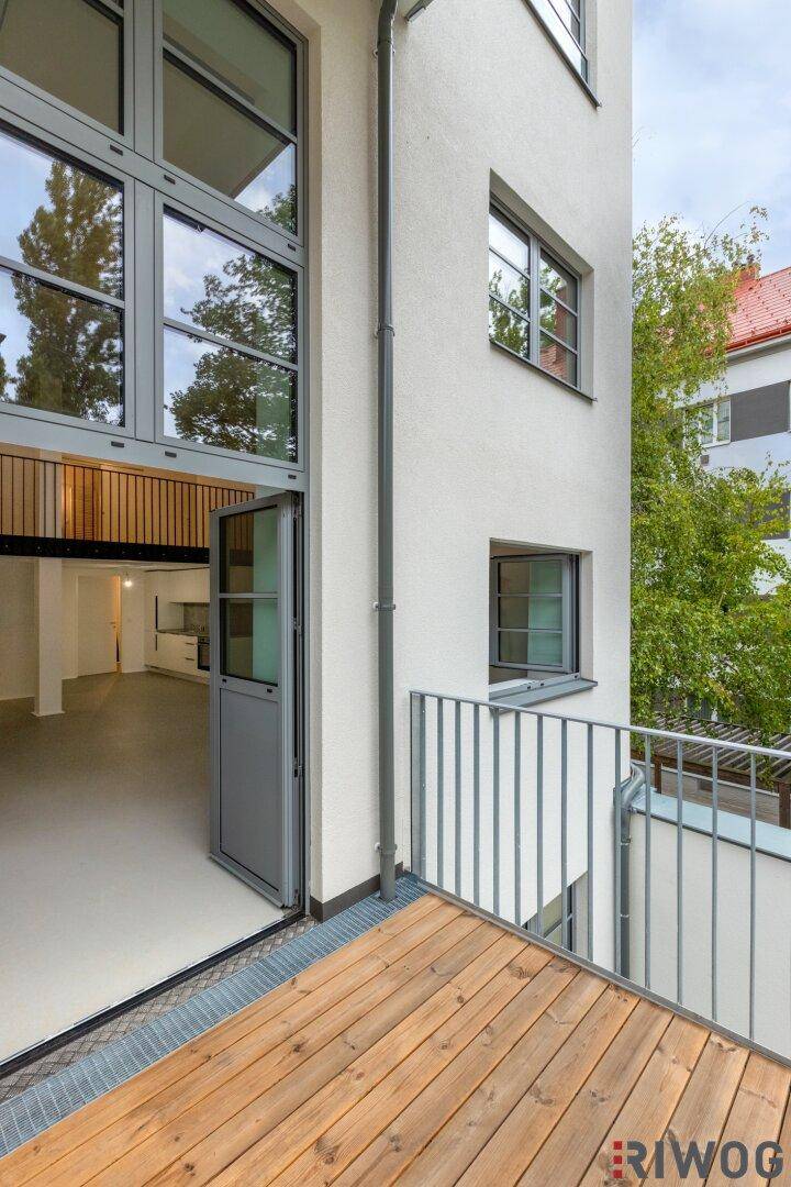 Balkon mit Holzboden und Blick auf die moderne Fassade und die umliegenden Bäume.
