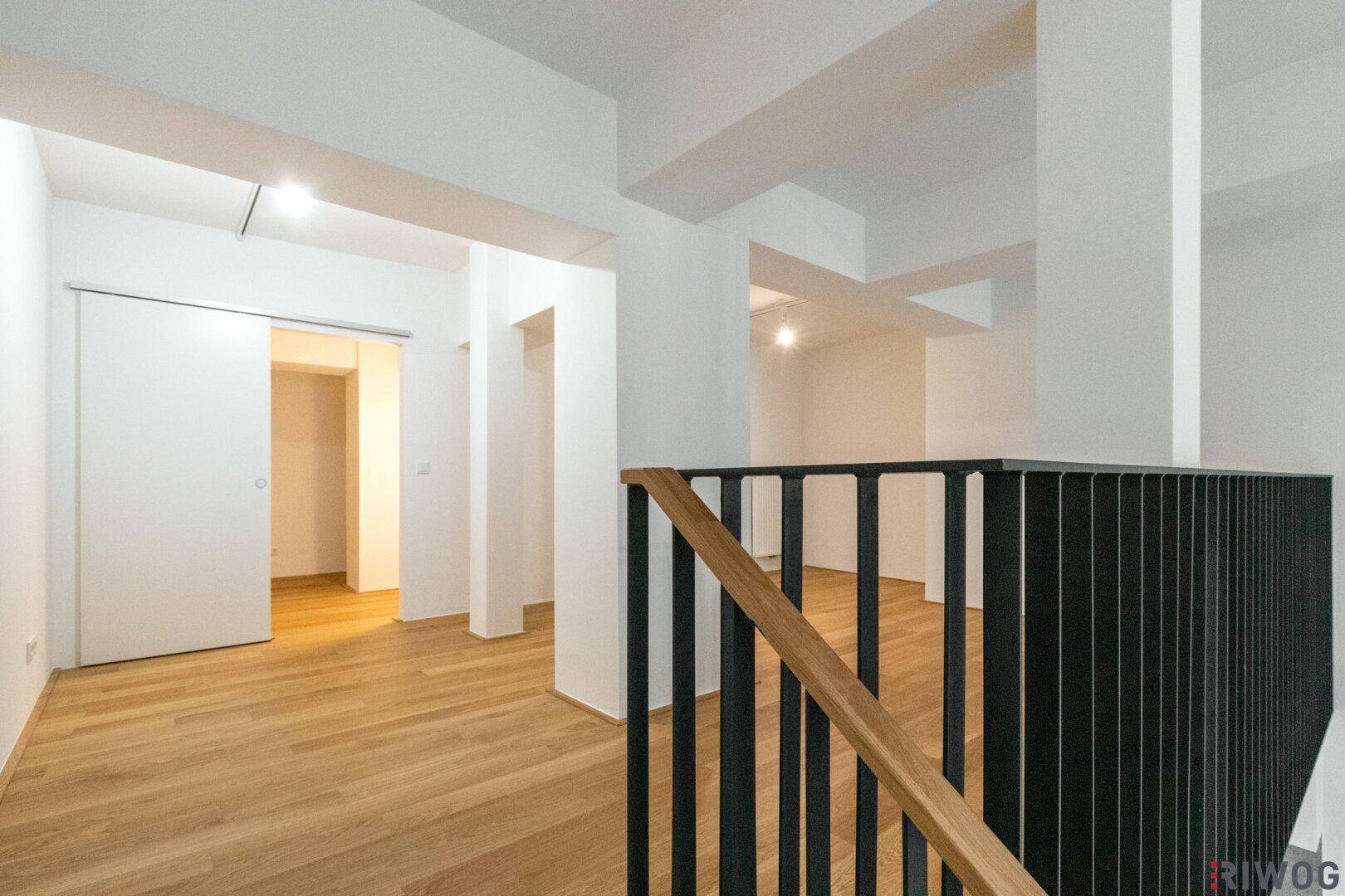 Heller Galeriebereich mit Holzfußboden und Schiebetür zu einem weiteren Raum.