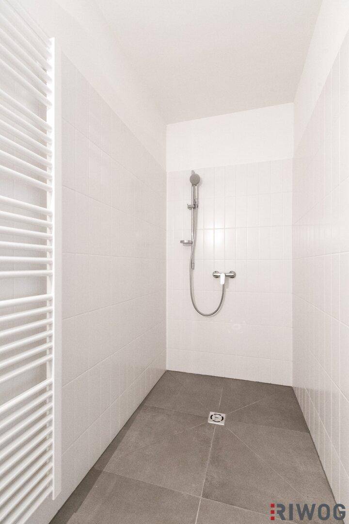 Ebenerdige Dusche mit modernen Fliesen und Duscharmatur in hellem Badezimmer.