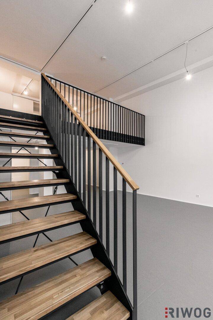 Moderne Holztreppe mit schwarzem Geländer führt zur oberen Galerieebene.