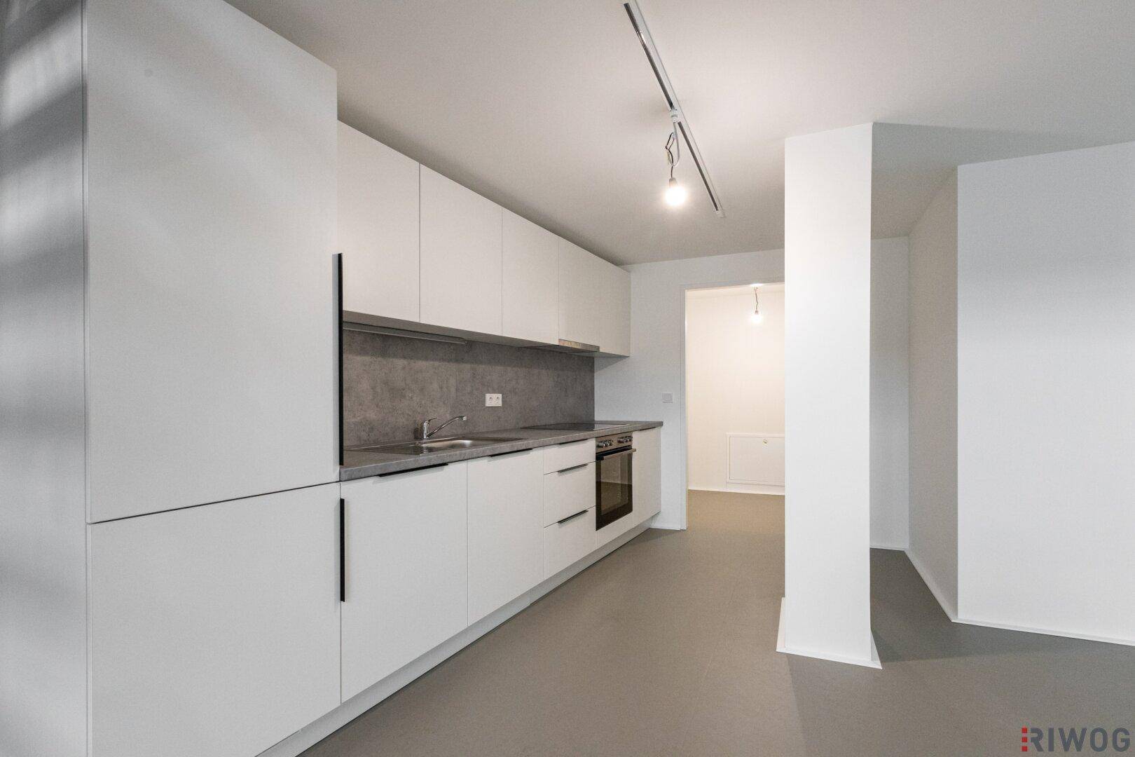 Moderne Küchenzeile mit weißen Schränken, grauer Arbeitsplatte und integriertem Backofen.