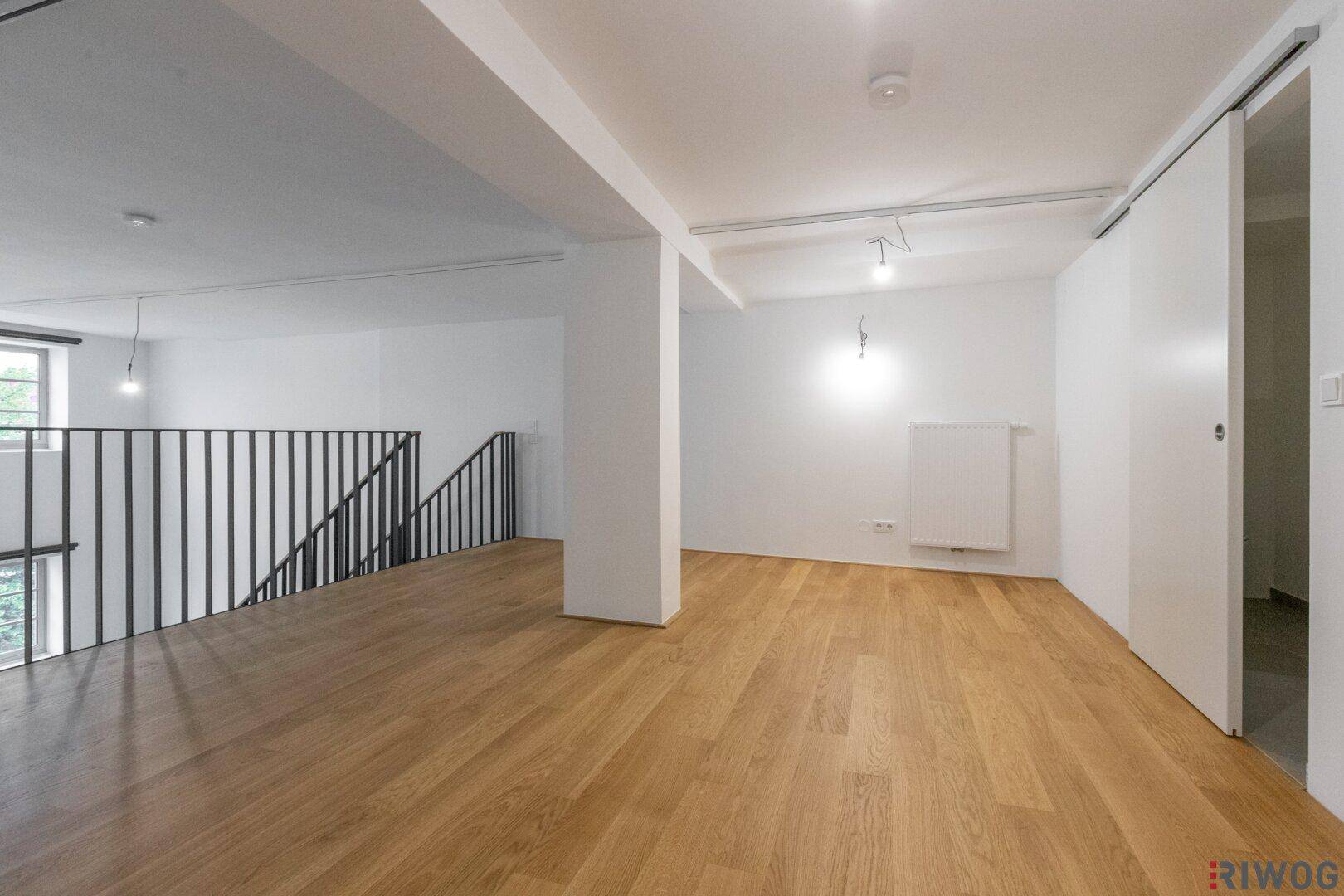 Helle Galerieebene mit Holzfußboden und moderner Schiebetür zu einem weiteren Raum.